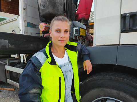 Mid adult caucasian female truck driver standing next to a truck and wearing reflective clothing.