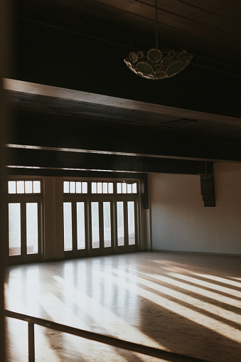 Afternoon light streaks through the windows of an empty room with wooden floors..