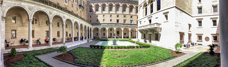 Boston, Massachusetts, USA - May 18, 2022: Panoramic view of the McKim Courtyard at The Boston Public Library. Charles Follen McKim designed the Central Library’s courtyard after that of the Palazzo della Cancelleria in Rome. Its covered arcade surrounds an open plaza skirted by white marble and low greenery, at the center of which lies a pool and fountain. The Boston Public Library contains approximately 24 million items, making it the third-largest public library in the United States behind the federal Library of Congress and the New York Public Library.