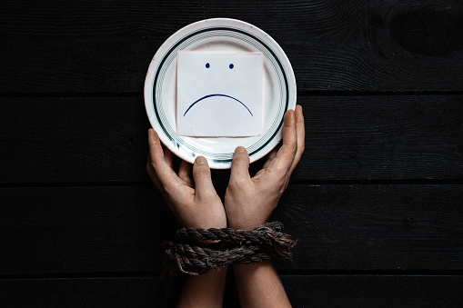 a plate with paper on which is drawn a sad smiley and women's hands tied with a rope, hunger and nothing to eat, slavery