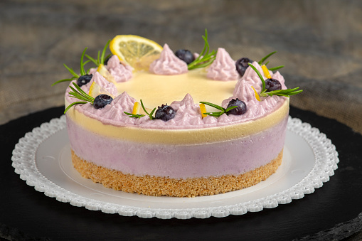 Blueberry cheesecake cake decorated with whipped cream and rosemary.\nCheese cream and yellow lemon glaze on a slate tray.