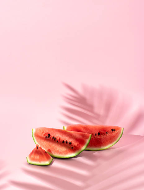 Creative Summer fruit party concept of refreshing watermelons under a palm tree. Pastel pink background.