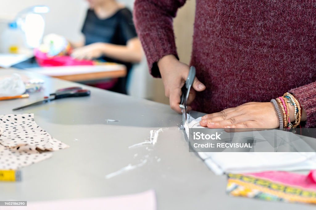 Woman seamstress in the workshop cutting a piece of cloth on a table. Woman seamstress cutting with scissors a piece of cloth on a table while in the workshop. Sewing concept Hand Stock Photo