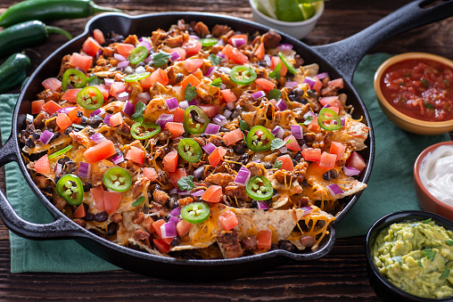 Fresh Nachos in a cast iron skillet, covered with jalapeno peppers, cheese, chicken, tomato and black beans.