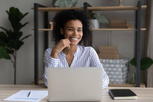 istock Happy dreamy young African woman working on computer in office. 1402192460