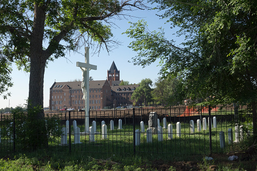 Built in 1891, the Romanesque red sandstone Loretto Heights Academy building stands in Denver County with the cemetery housing the passed Sisters of Loretto in the foreground. The old Catholic boarding school for girls has gone under construction that will repurpose the entire campus for apartments and housing and relocate the cemetery.