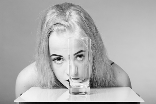 girl looks at camera through glass with water on gray background, monochrome