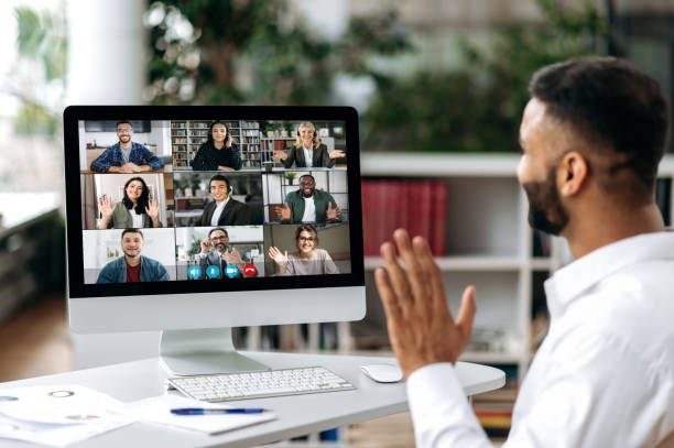 istock Video call, online conference. Over shoulder view of Indian man, on computer screen, talks with multinational group of successful business people, virtual business meeting, telecommunication concept 1402198715