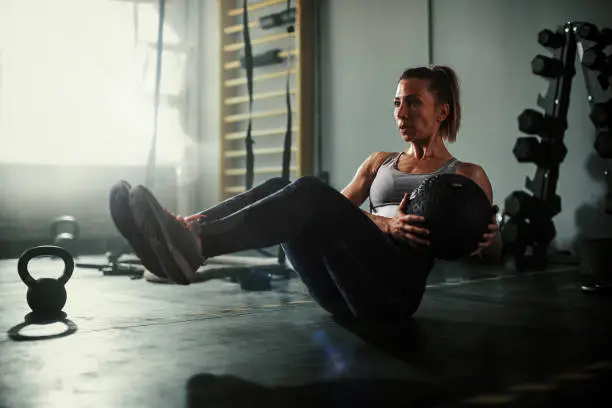 A beautiful and strong athletic young woman working hard cross fitness workout in low light gym working with medicine ball.