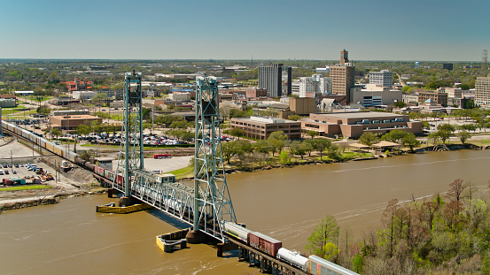 Aerial establishing shot of a freight train crossing the Neches River in Beaumont, Texas on a clear sunny afternoon.