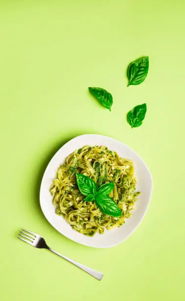 Tagliatelle pasta with pesto sauce, basil and pine nuts on light green background. Italian cuisine. Top view. Flat lay minimalist design.