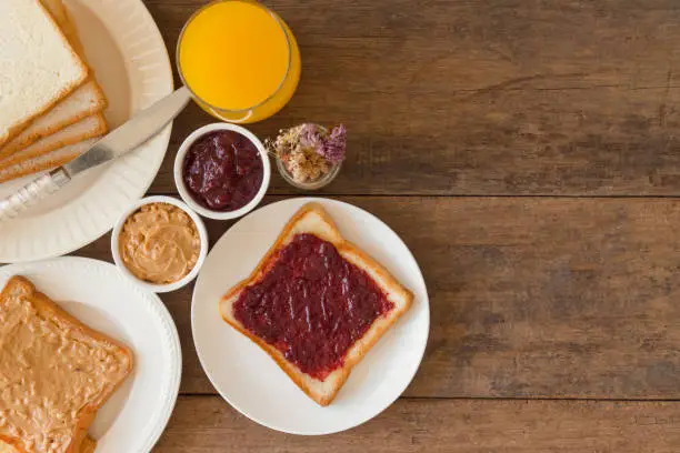 Toast bread with homemade strawberry jam and peanut butter served with orange juice. Homemade toast bread with jam and peanut butter on table for breakfast. Delicious toast bread in top view flat lay.