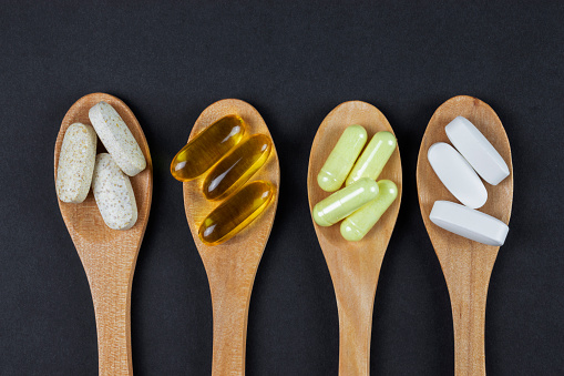 Vitamins and herbal supplements and pills on four wooden ecological spoons and balck background