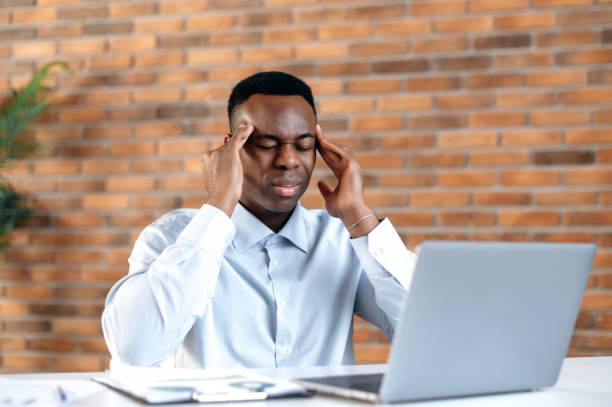 istock Migraine, fatigue. African American office worker, manager, programmer, tired of working at a laptop in the office, having a headache, massaging temples, closed his eyes, needs rest 1402203765