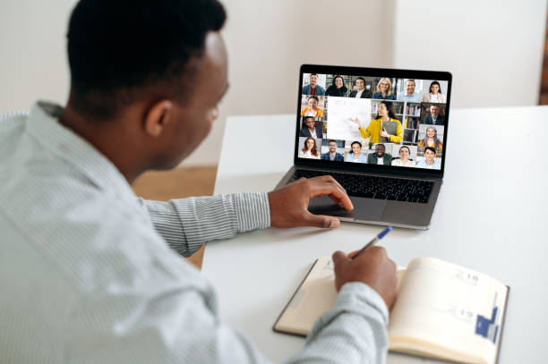 istock Online learning. African American smart guy, student or freelancer, sit at a table at home in the kitchen, has an online webinar, lecture, takes notes, on the screen group of multiracial people 1402203844