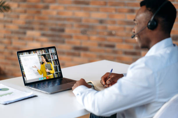istock E-learning. Successful smart young african american man, looking at laptop screen, listening online lecture by video conference, taking notes during virtual webinar, brainstorming, improving skills 1402203861