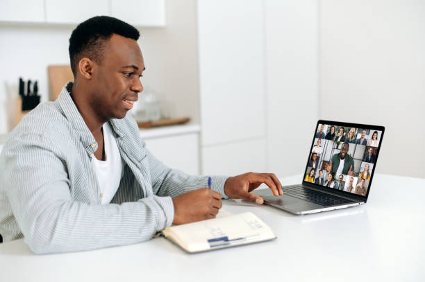 istock Smart positive african american man sits at a table at home, using a laptop, takes part in a multi-rice video conference with colleagues or employees, takes notes. E-learning concept. Work from home 1402203907