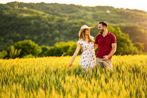 Beautiful couple walking outdoors on a field during sunset.