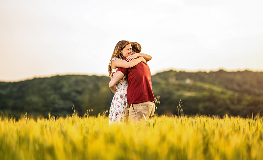 Carefree couple embracing while standing outdoors on a gold colored field.