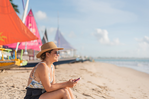 Woman sitting on beach sand using cellphone
