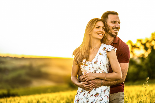 Beautiful couple embracing while standing outdoors on a gold colored field.