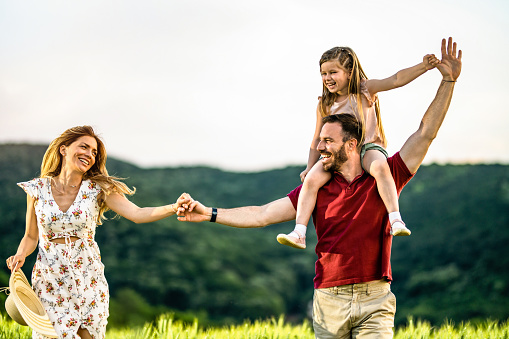 Playful parents having fun with their little girl while walking on a field.