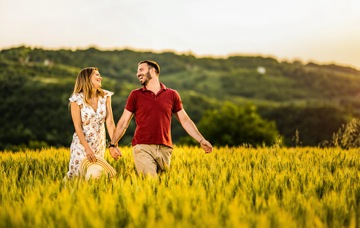 Carefree couple holding hands while walking outdoors on a field during sunset.