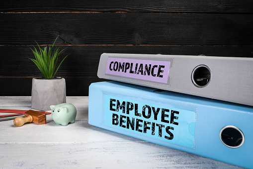 EMPLOYEE BENEFITS and COMPLIANCE. Document binders, folders on a wooden office desk.
