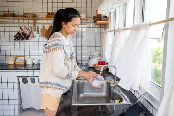 woman washing dishes A woman in a sweater is washing dishes in the kitchen. asian woman cleaning dishes stock pictures, royalty-free photos & images
