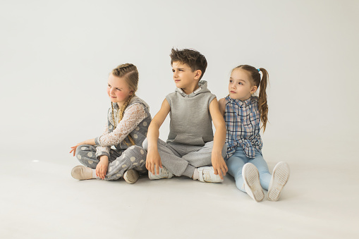 Two girls and boy in light clothes are sitting on white background in studio. Baby tooth. Happy childhood. Preschool age. Cheerful children. Playful girl. Middle eastern boy