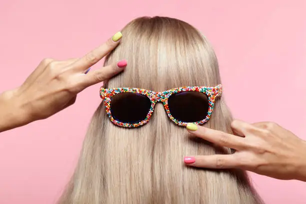 Rear view of young woman. Blond stright hair with fun sunglasses.Female finger nails with bright manicure