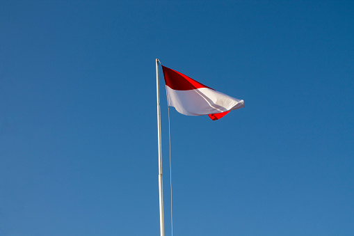 Indonesian national flag (red and white) flying against a blue sky background. Flags are flown on independence celebrations and other days in government and private buildings