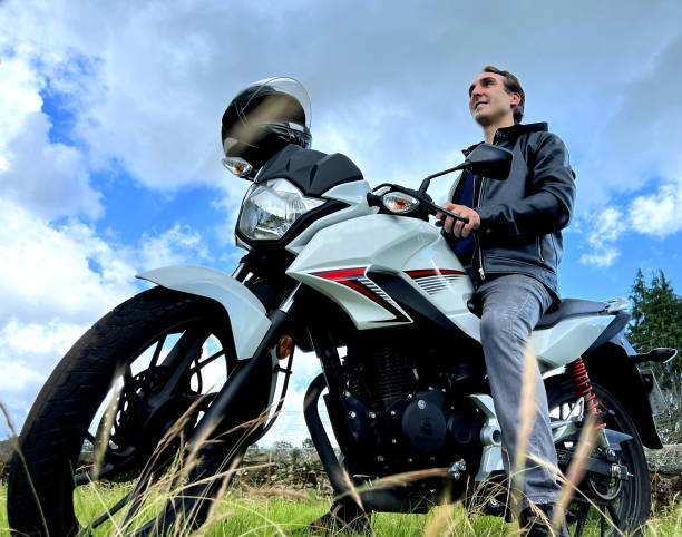 um homem adulto de 30 a 45 anos senta-se contra o céu na moto e olha para a distância uma moto branca e um homem tem uma jaqueta preta e jeans preto um bom anúncio para reclax e viagens - 30 35 years fotos - fotografias e filmes do acervo