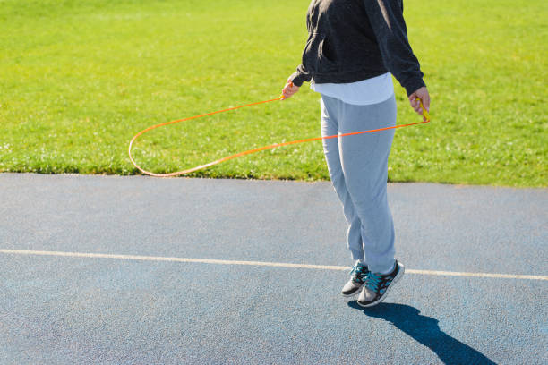 Unrecognizable overweight woman jumping rope, sportswoman exercising cardio at outdoor sports ground on sunny day, copy space. Fitness, aerobics and weight loss concept. stock photo