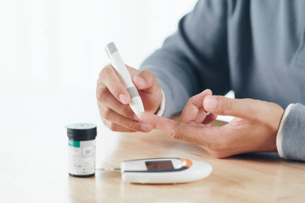 グルコースメーター、ヘルスケアと医療、糖尿病、糖血症の概念によって血糖値をチェックするために指にランセットを使用してアジア人男性 - 糖尿病 ストックフォトと画像