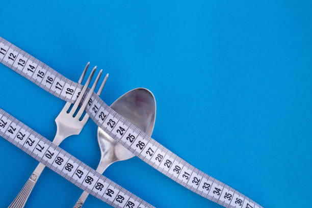 White centimeter, fork and spoon  on the blue background. Top view. Copy space. Close-up.