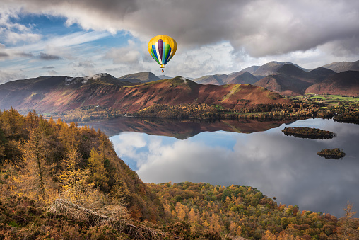 Digital composite image of hot air balloons over Epic landscape Autumn image of view from Walla Crag in Lake District, over Derwentwater looking towards Catbells and distant mountains