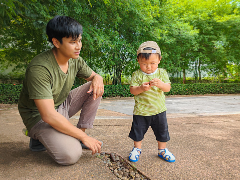 Young Asian father and baby son enjoy walking and playing together at the park outdoors, Family relaxing and spending time with their children outside in green nature