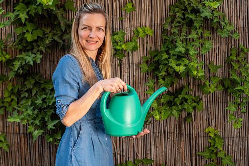 Happy woman holding bucket with water to watering flowers in the yard