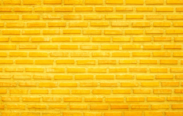 istock Brick wall painted with yellow paint pastel bright tone texture background. Brickwork and stonework flooring interior with rock old pattern clean grid concrete uneven bricks design backdrop. 1402260054