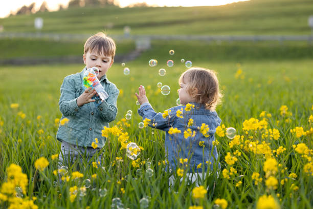 ragazzo e una ragazza giocano con le bolle di sapone in un prato - huckleberry finn foto e immagini stock
