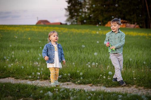 a boy and a girl catch soap bubbles in a summer meadow