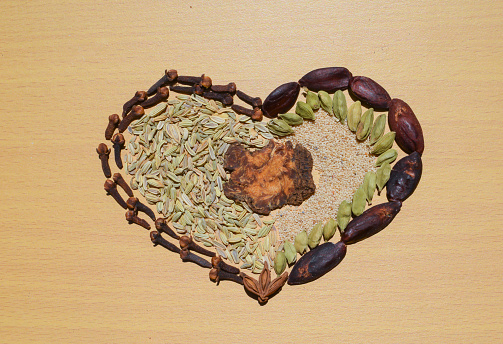 Composition of condiment making heart shape. Cuisine and flavouring concept. Set of spices on wooden brown texture background. Seasoning \