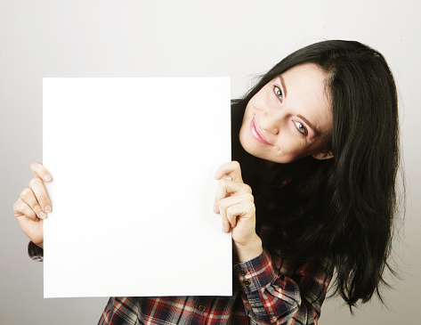 Smiling young casual style woman showing blank signboard, over grey background isolated