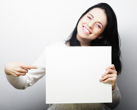 Smiling young casual style woman showing blank signboard, over grey  background isolated