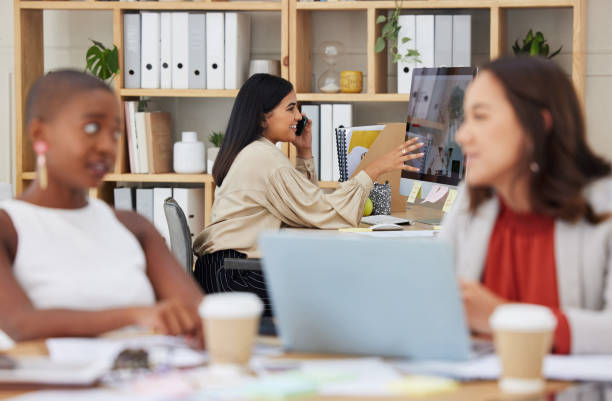 istock Serious ambitious indian business woman using cellphone to talk to clients while using office computer. Confident ethnic professional sitting behind team, explaining and sharing ideas while networking 1402278508