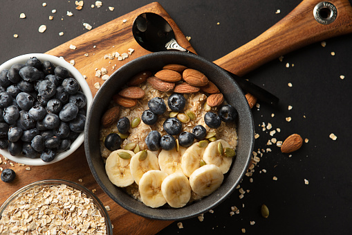 Above view of Healthy Oatmeal bowl with banana and blue berries topping on wooden cutting board  on grey background.