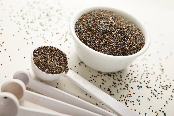 Measuring spoon with a small white bowl of chia seeds on quartz counter top
