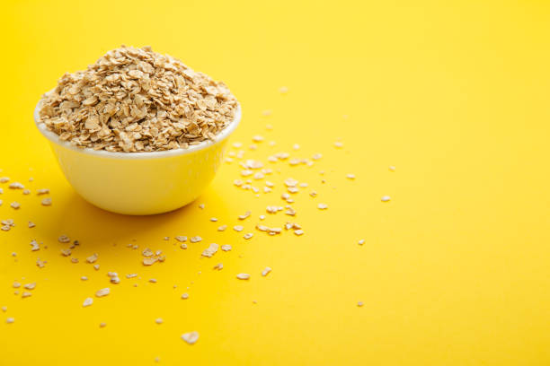 Over flowing oatmeal flakes bowl on yellow background.