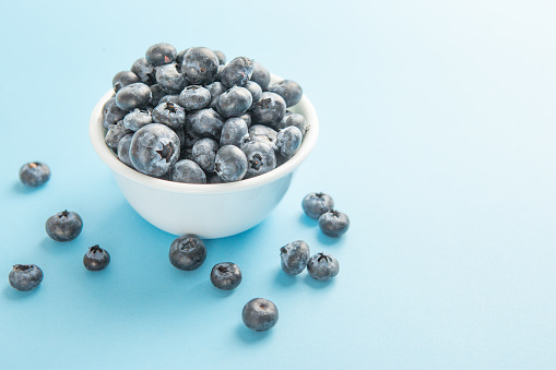 Over flowing white bowl of blueberries on blue background.